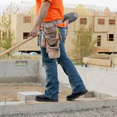  A construction worker walks along a concrete foundation, wearing the black Boss 11” Comp Toe Men’s Work Boot. The sturdy, protective boot is highlighted as the worker, dressed in an orange shirt and tool belt, handles a shovel on a busy construction site with wooden structures in the background. The boots emphasize durability and support for demanding job sites.