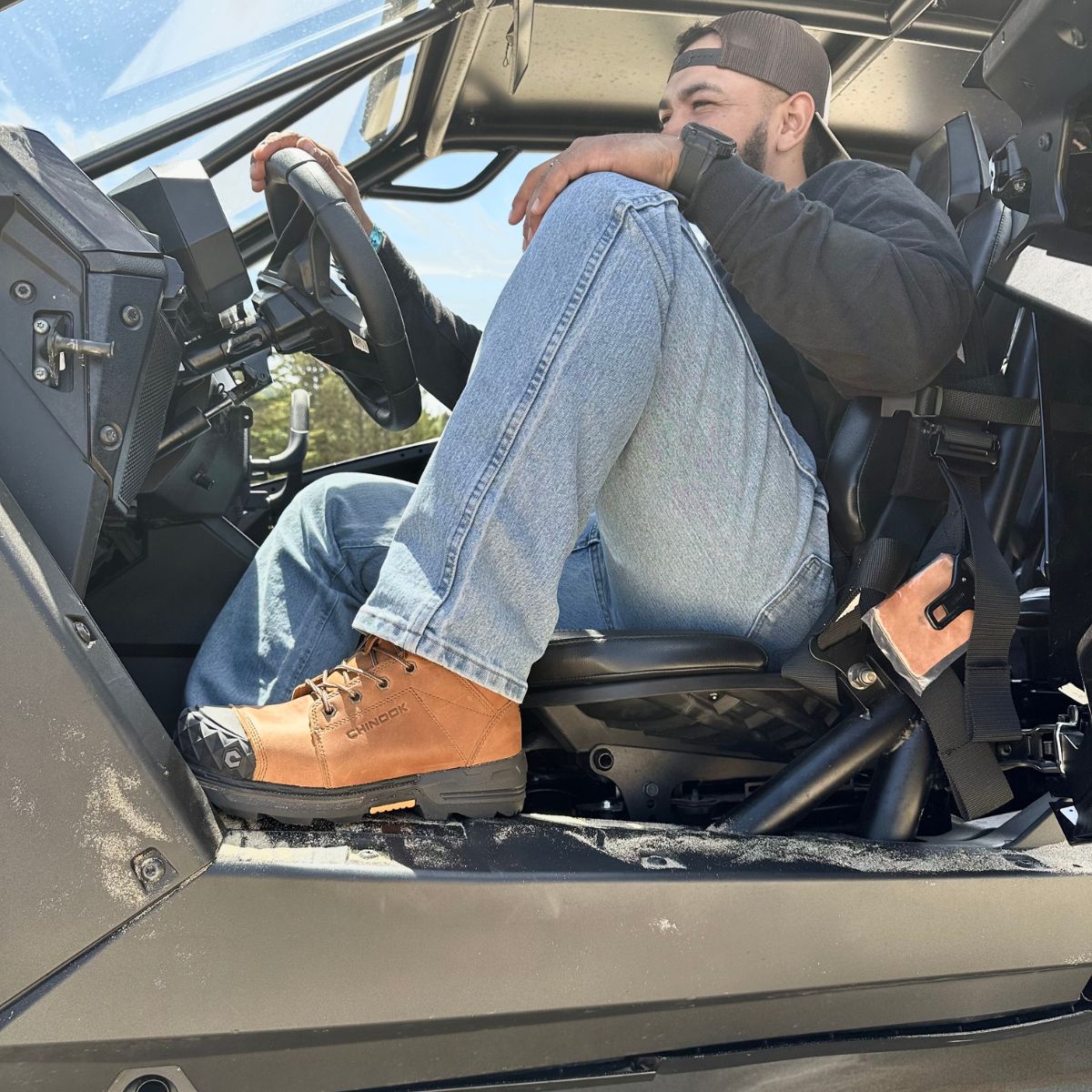 A man wearing Maverick 6” Comp Toe Men’s Waterproof Work Boots in wheat color relaxes in an off-road vehicle, with one foot casually propped on the side rail. These rugged boots, designed with reinforced toes, are built to handle it all—whether you're tackling tough outdoor terrain or powering through a long day on the job.
